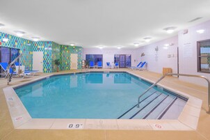 Una piscina interior con agua cristalina, un muro con azulejos de un diseño colorido y un cartel con las normas de la piscina.
