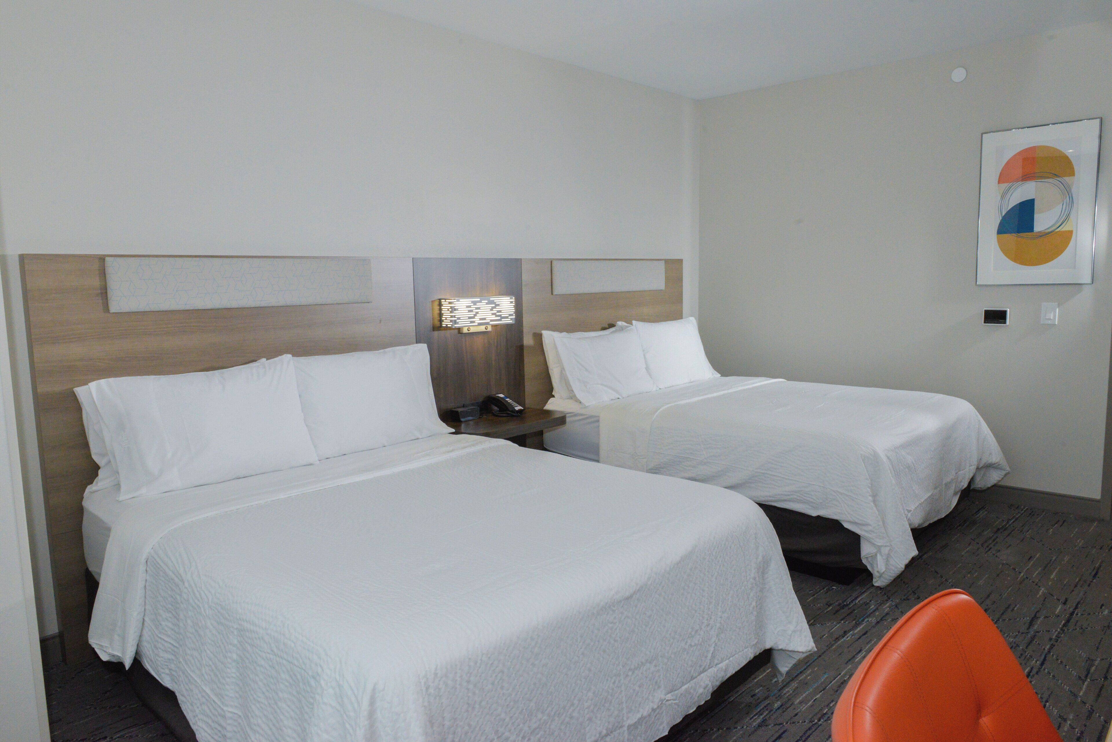 A hotel room with two beds, a nightstand, a lamp, and a framed artwork on the wall.