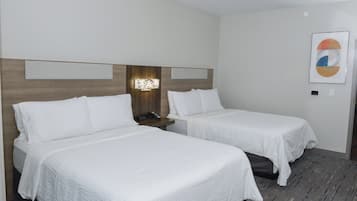 A hotel room with two single beds, a wooden headboard, a nightstand with a phone, and a framed abstract artwork on the wall.