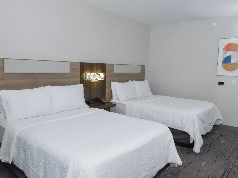 A hotel room with two single beds, a wooden headboard, a nightstand with a phone, and a framed abstract artwork on the wall.