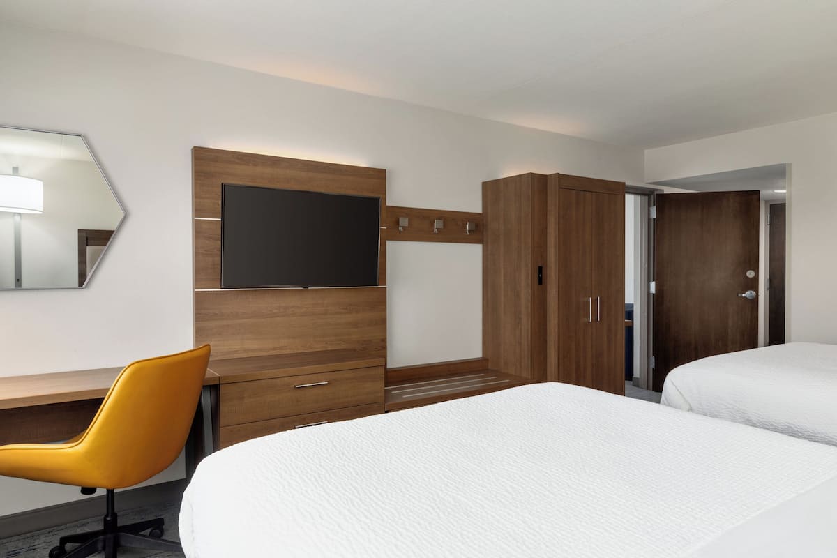 A hotel room with a bed, a desk with a chair, a wardrobe, a television, and a mirror.