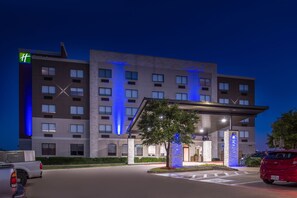 Un hotel con fachada moderna, un acceso cubierto y un área de estacionamiento.