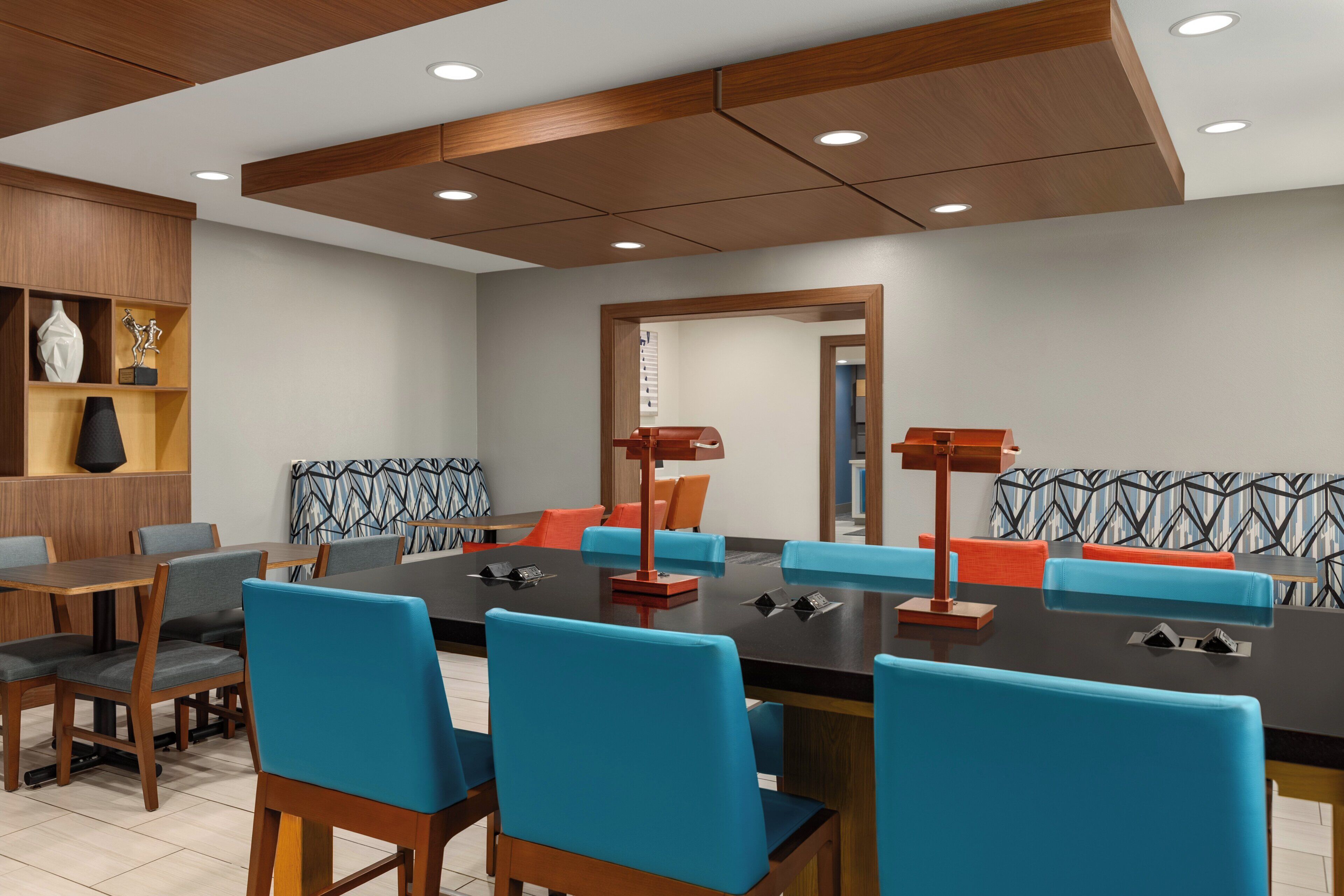 A modern meeting room with a long table, blue and orange chairs, wooden accents, and recessed ceiling lighting.