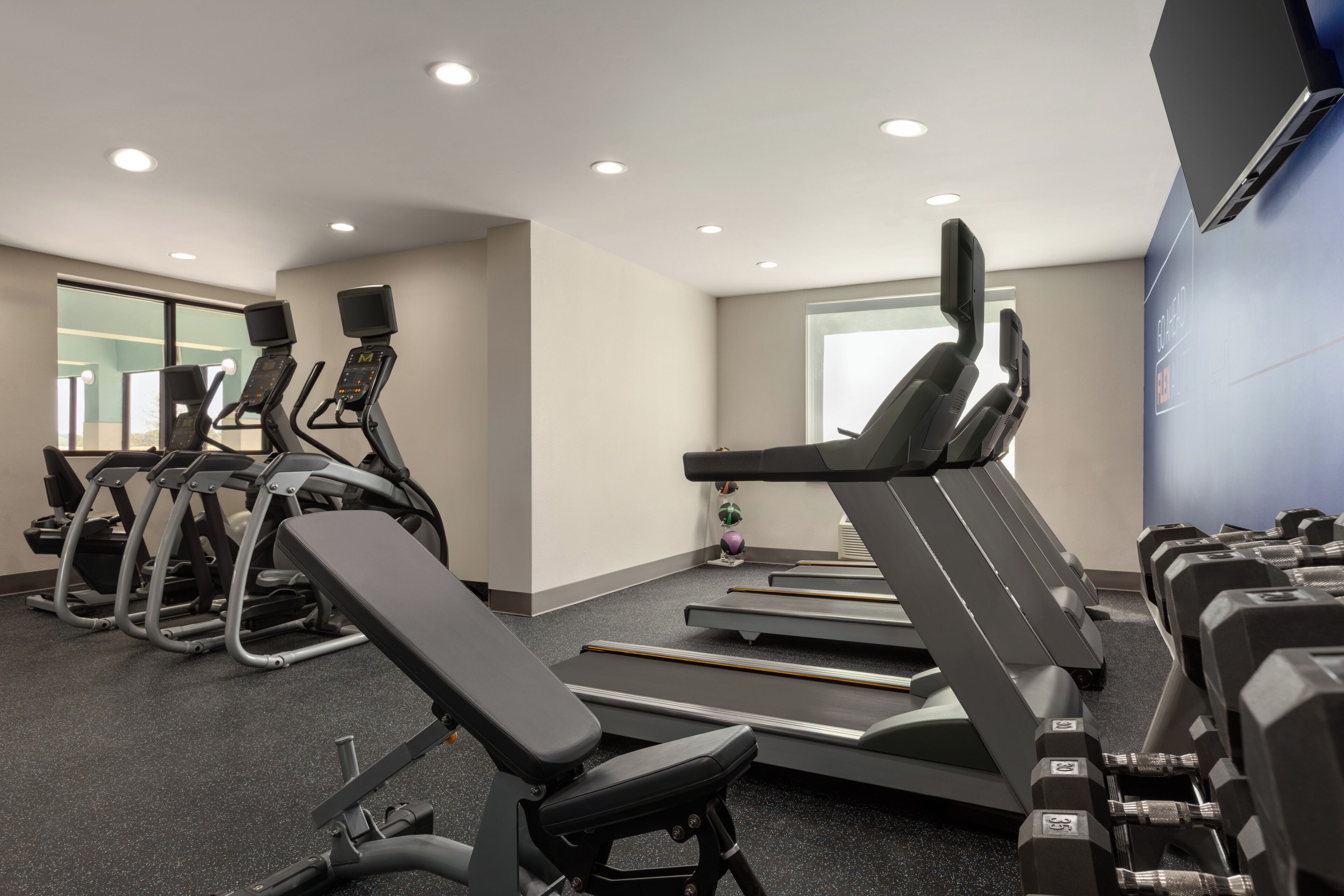 Un gimnasio con cintas de correr, elípticas y bancos de pesas.