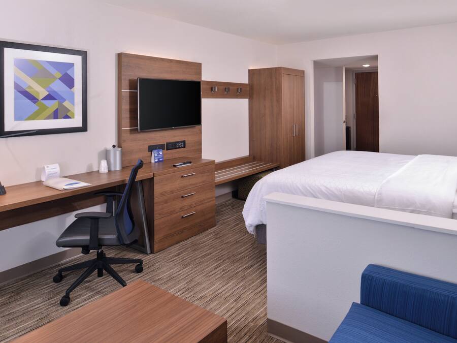 Une chambre d’hôtel comprenant un lit, un bureau avec une chaise, une télévision, une armoire et un tableau encadré au mur.