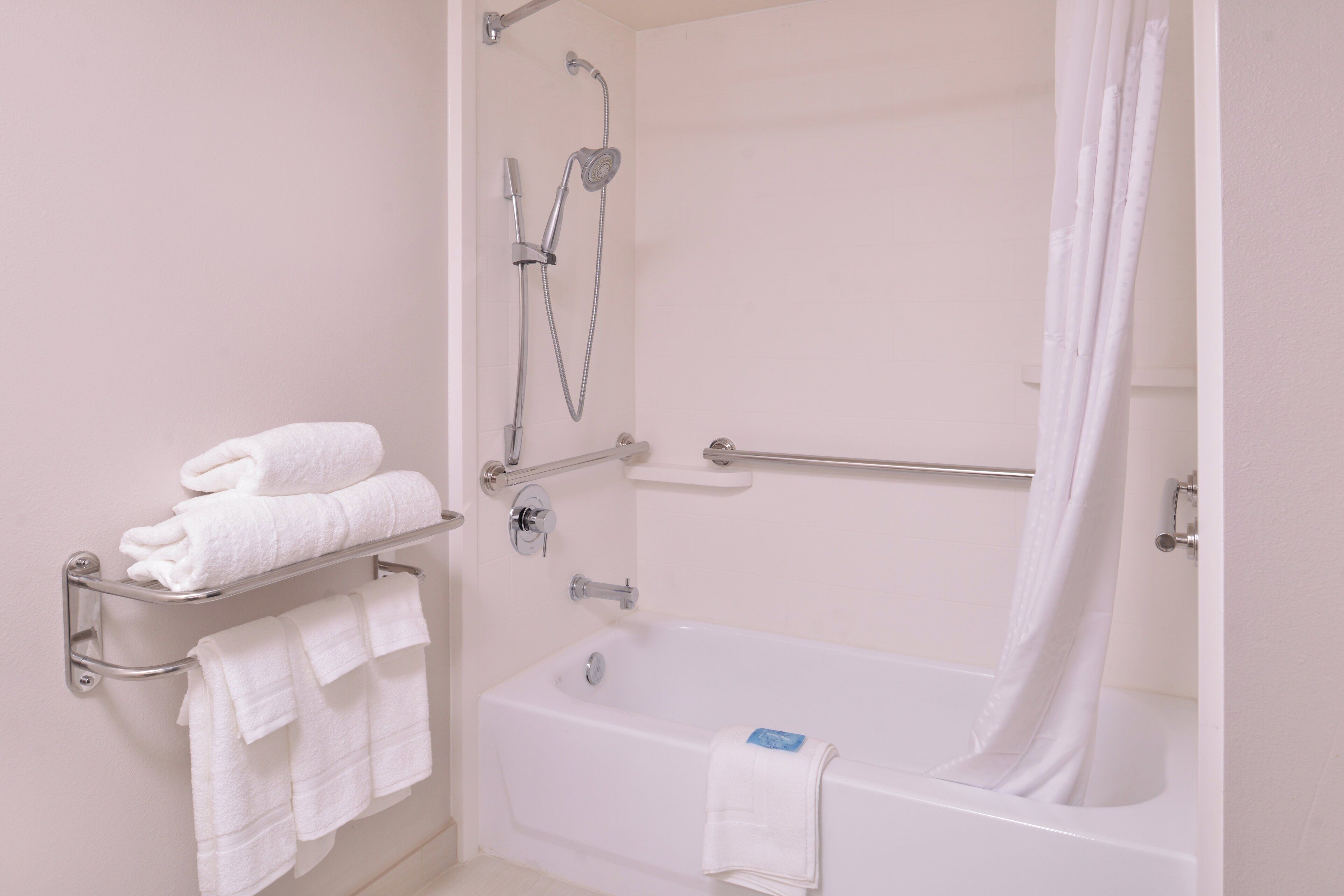 A bathroom with a bathtub, a shower, and a towel rack with folded towels.