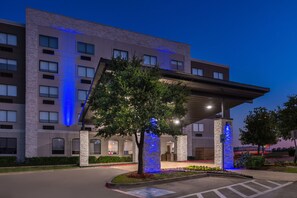 Una entrada de hotel moderna con un corredor cubierto, un pilar de piedra y un árbol.
