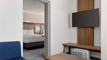 Una habitación de hotel con una cama, un televisor montado en la pared, un escritorio de madera y un sofá azul.