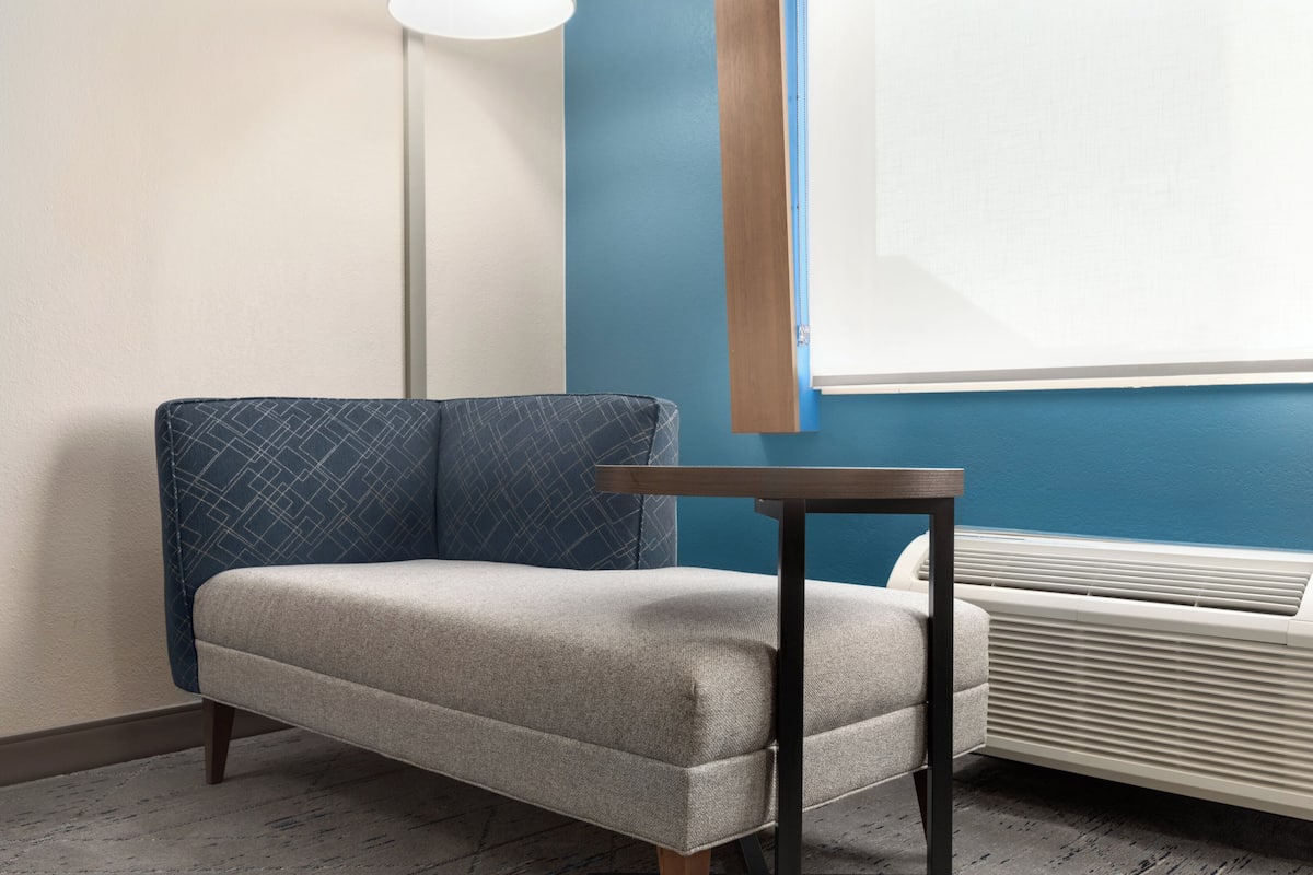 A room with a sofa, a table, a standing heater, and a window with blinds.