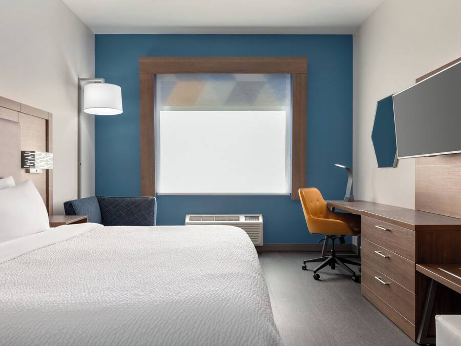 Quarto de hotel com cama, escrivaninha, cadeira, televisão e janela.