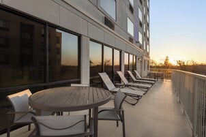 Un balcón con una mesa redonda y sillas, ventanas amplias y vistas al atardecer.