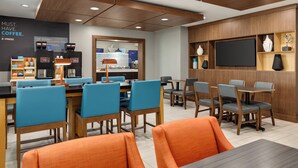 Een moderne hotellobby met een koffiebar, een zithoek en een flatscreen aan de muur.