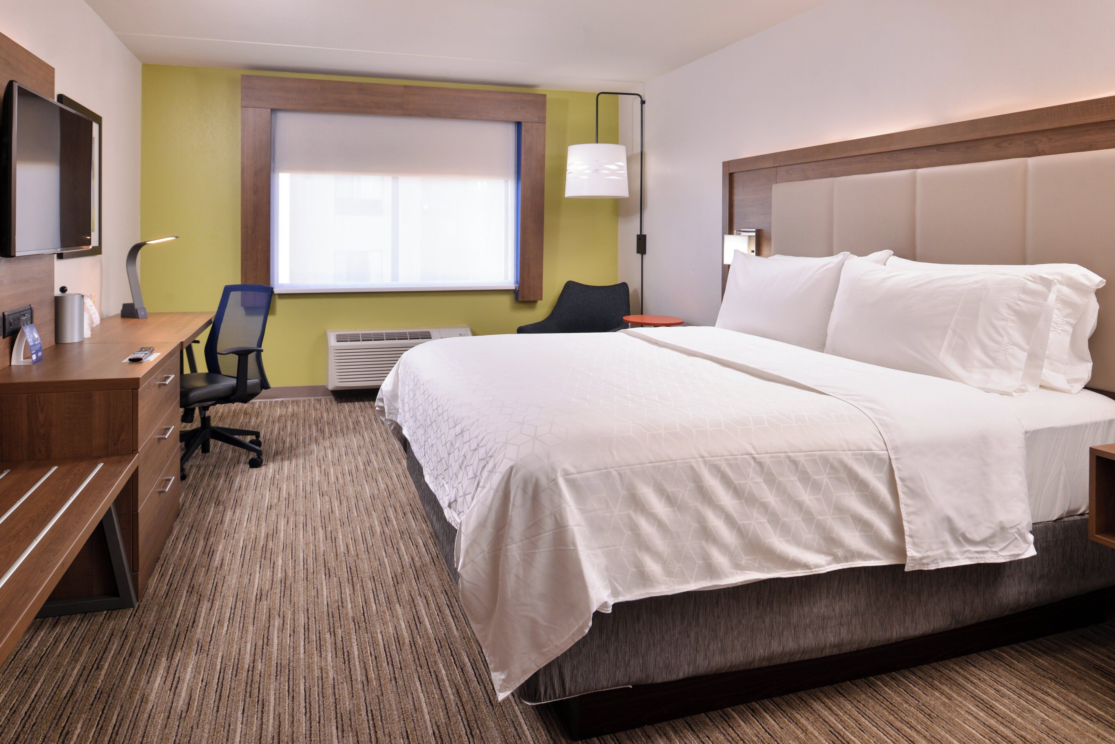 Quarto de hotel com cama, escrivaninha, cadeira e televisão.