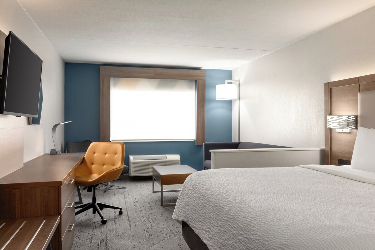 A hotel room with a bed, desk, chair, and a TV mounted on the wall.