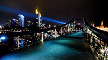 Une vue nocturne d’une ville, avec un pont dont les garde-corps sont illuminés, et une perspective sur les bâtiments qui composent son profil.