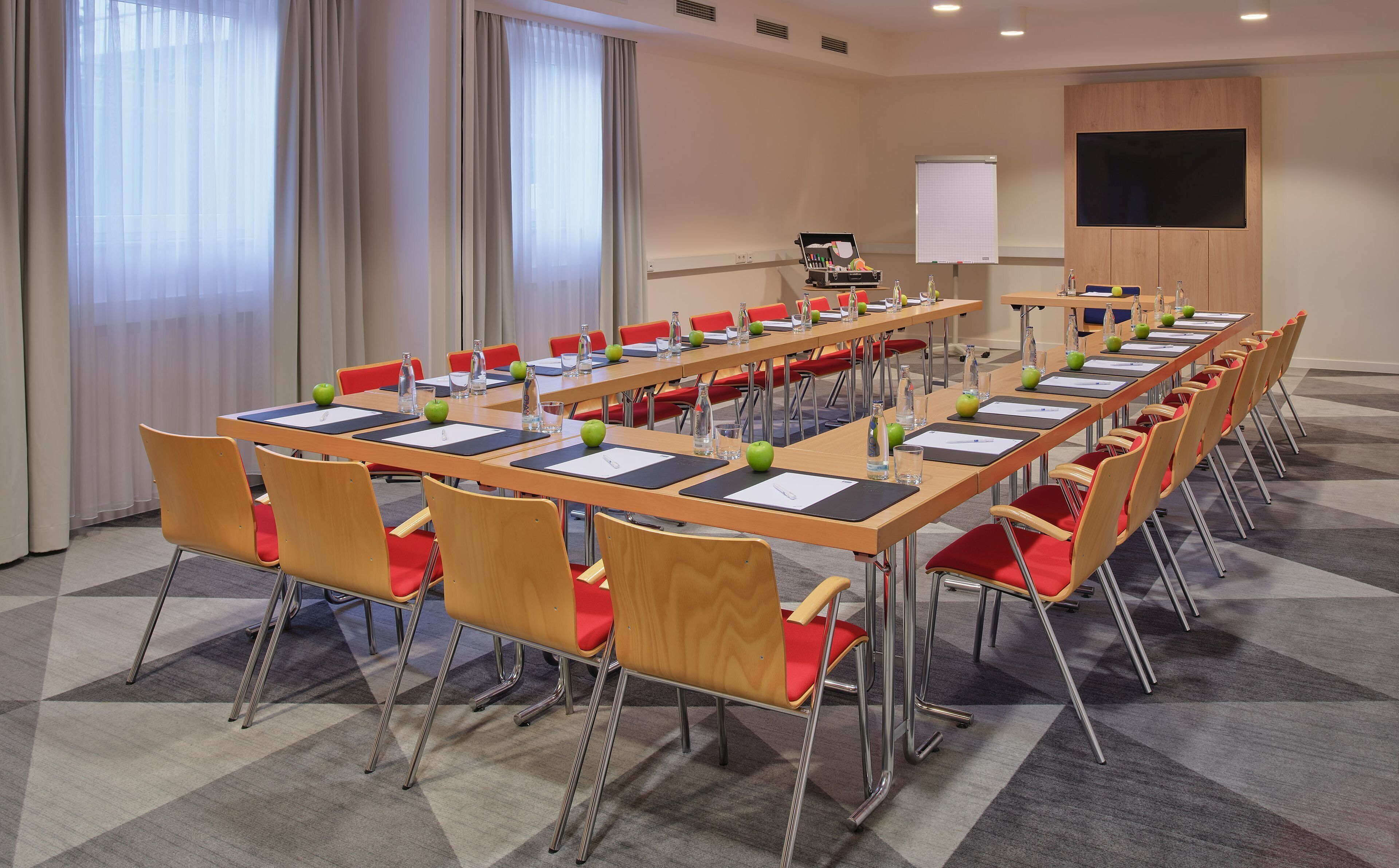 A conference room with long tables, red chairs, and a whiteboard.