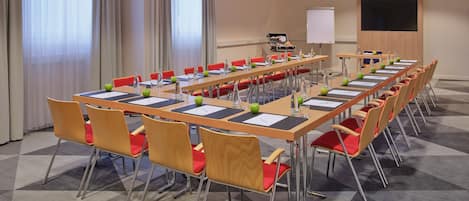 A conference room with long tables, red chairs, and a whiteboard.