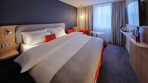 A hotel room with a large bed, a desk, a TV, and a window with curtains. - Holiday Inn Express Frankfurt Airport by IHG (Moerfelden-Walldorf)