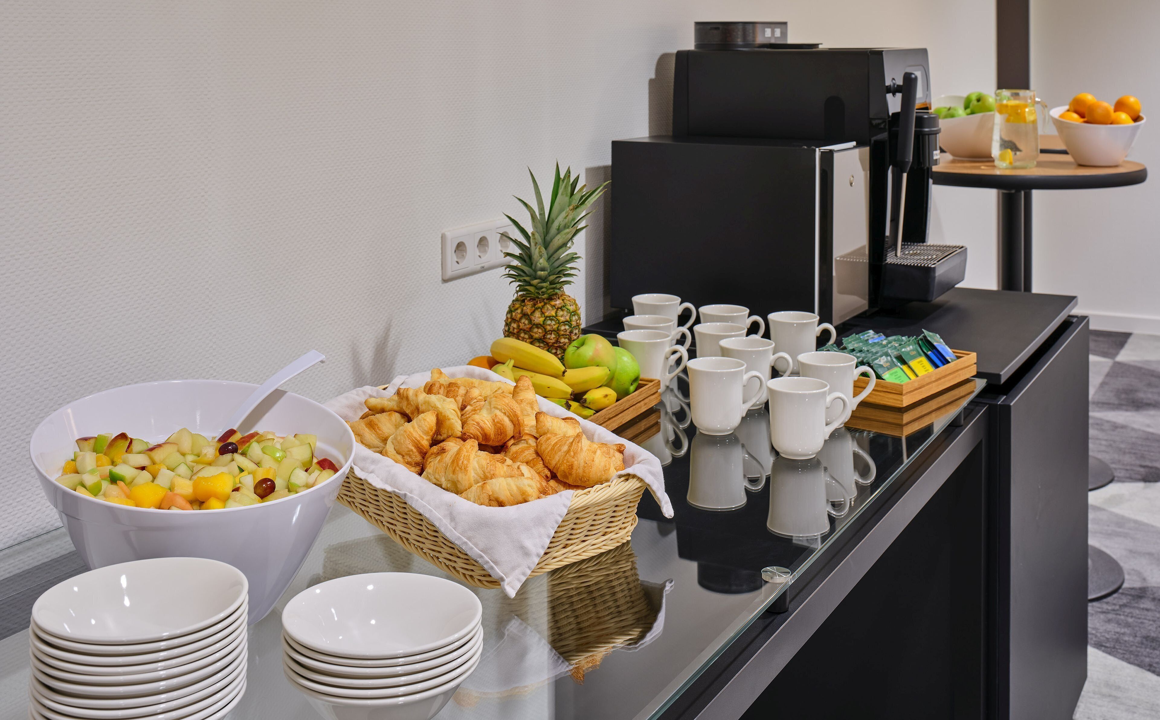 A buffet table with fruits, pastries, and coffee cups.