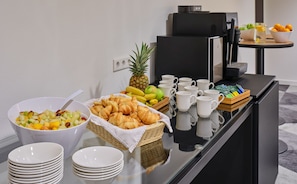 Una mesa de buffet con frutas, pasteles y tazas de café.