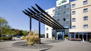 Et hotelindgangsparti med et moderne design, inklusive et overdækket udendørs område med siddepladser og en anlagt have.