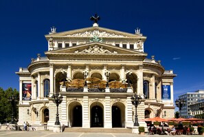 Un bâtiment de style classique, doté d’un balcon central, de colonnes richement décorées et d’une statue sur le toit.