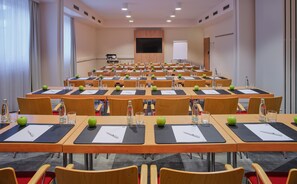 A conference room with rows of tables, chairs, and a large screen at the front. - Holiday Inn Express Frankfurt Airport by IHG (Moerfelden-Walldorf)