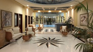 Een hotellobby met een centraal zitgedeelte, uitzicht op een zwembad en een plafondschildering.