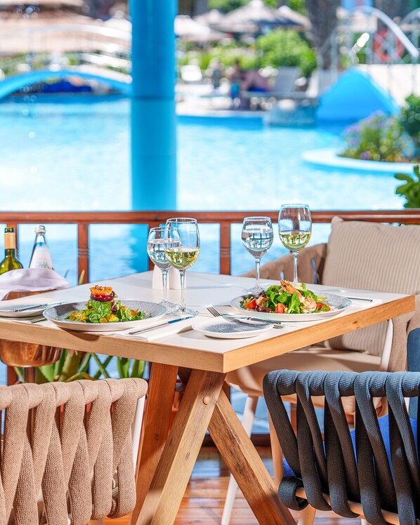 A dining table set with plates, glasses, and cutlery, overlooking a pool area.
