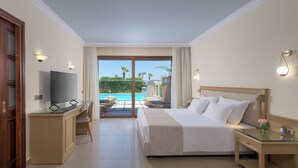 Een hotelkamer met een bed, bureau, televisie en uitzicht op een zwembad en palmbomen.
