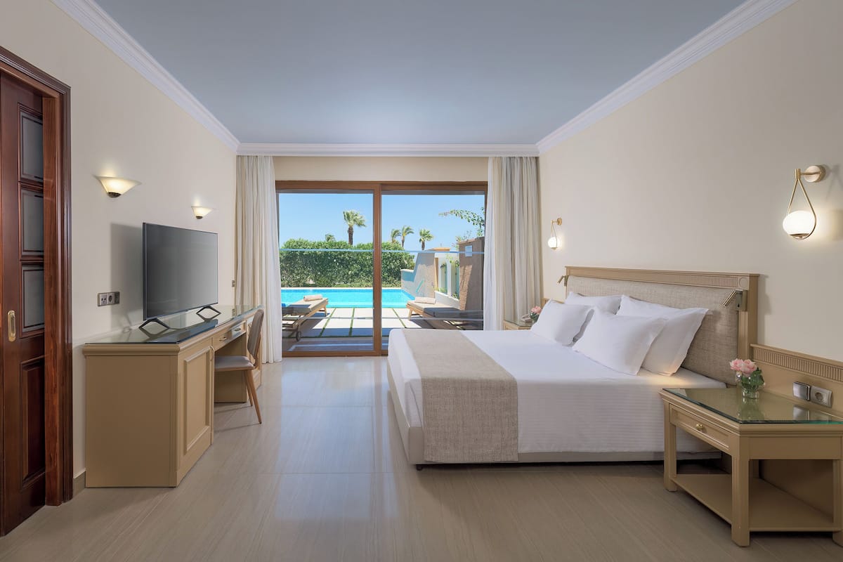 Ein Hotelzimmer mit Bett, Schreibtisch, Fernseher und Blick auf einen Pool und Palmen.