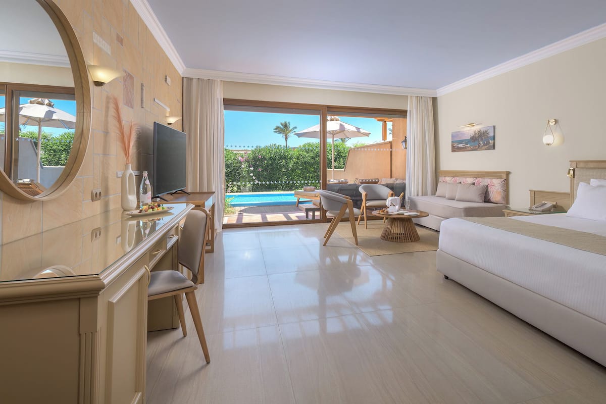 Ein Hotelzimmer mit Bett, Schreibtisch mit Stuhl, Fernseher und Blick auf Pool und Grünflächen.