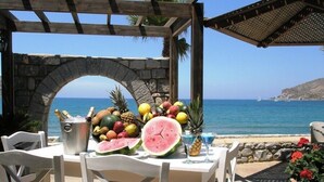 A table set with fruits, a bottle of champagne, and a drink, overlooking a coastal view. - Itilo Traditional Hotel (East Mani)