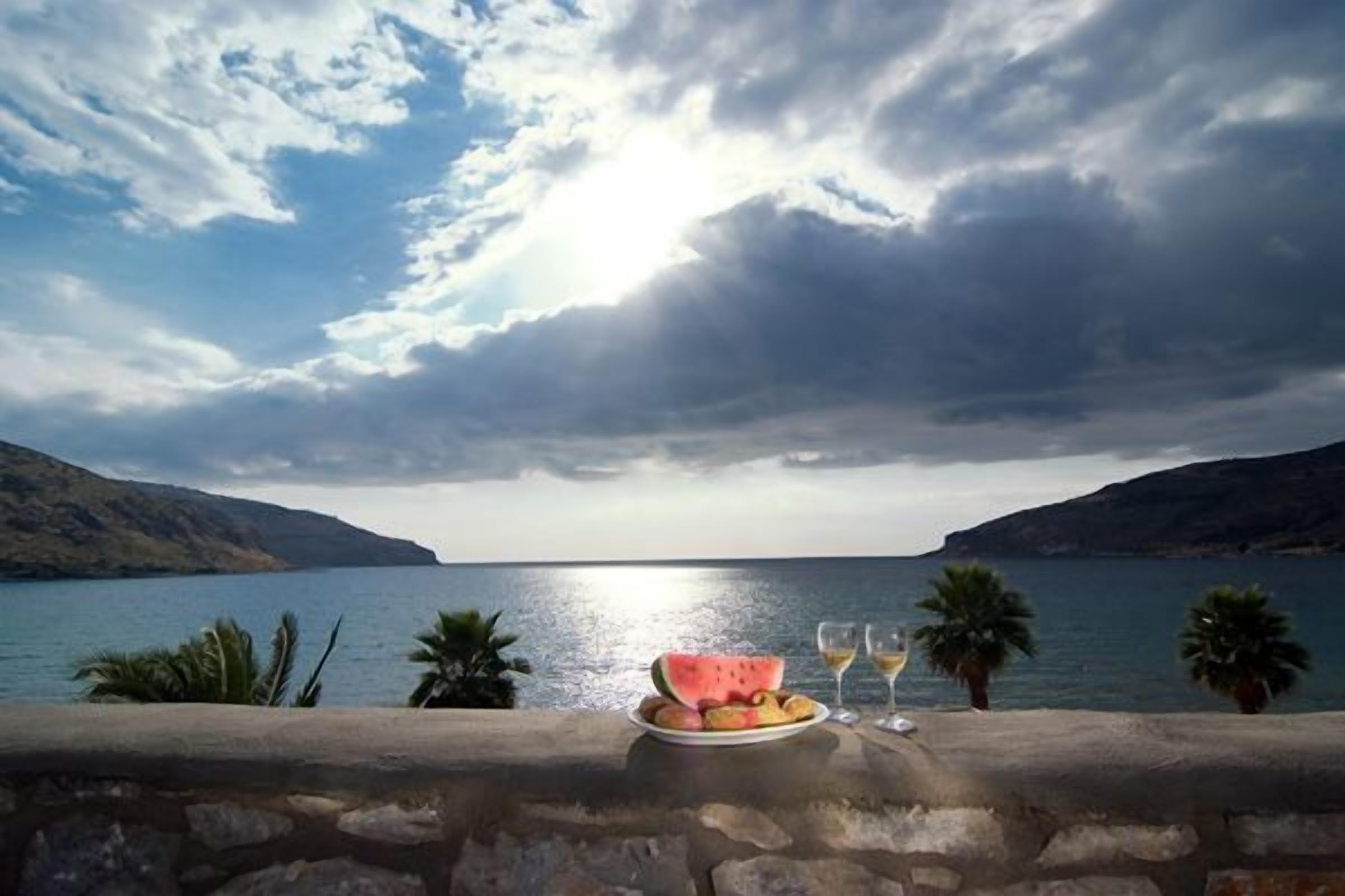 A scenic view of a coastal landscape with a stone wall, a plate of fruit, and two glasses of wine.