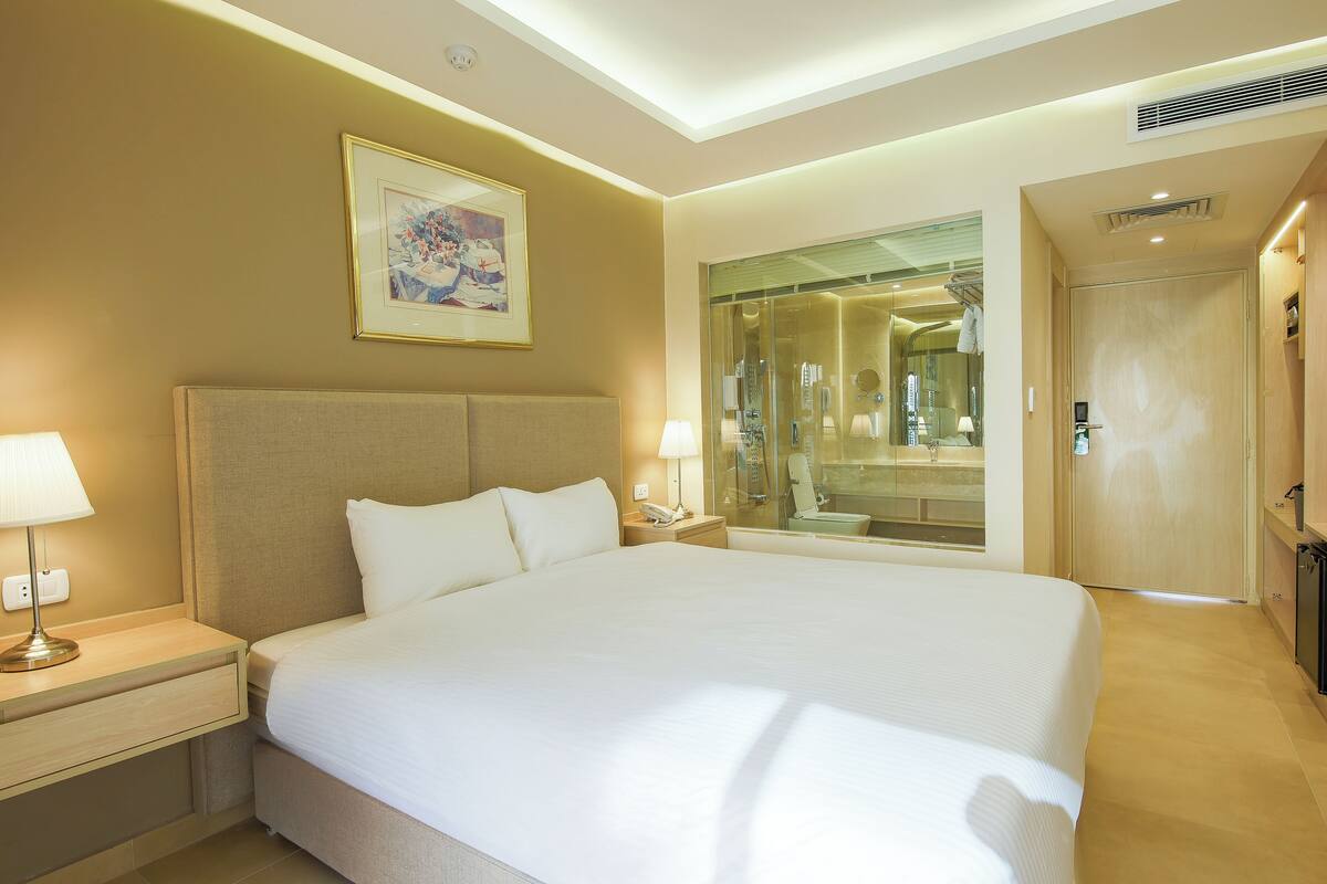 A hotel room with a large bed, bedside lamps, a painting on the wall, and a mirror reflecting the bathroom.