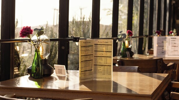 A restaurant interior with a wooden table, chairs, a menu stand, and a view through a glass wall. - Petra Palace Hotel (Wadi Musa)