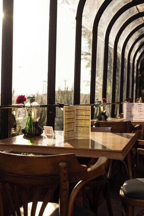 A restaurant interior with a wooden table, chairs, a menu stand, and a view through a glass wall. - Petra Palace Hotel (Wadi Musa)