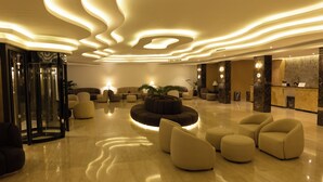 A modern lobby with a central seating area, a reception desk, and a glass elevator. - Petra Palace Hotel (Wadi Musa)