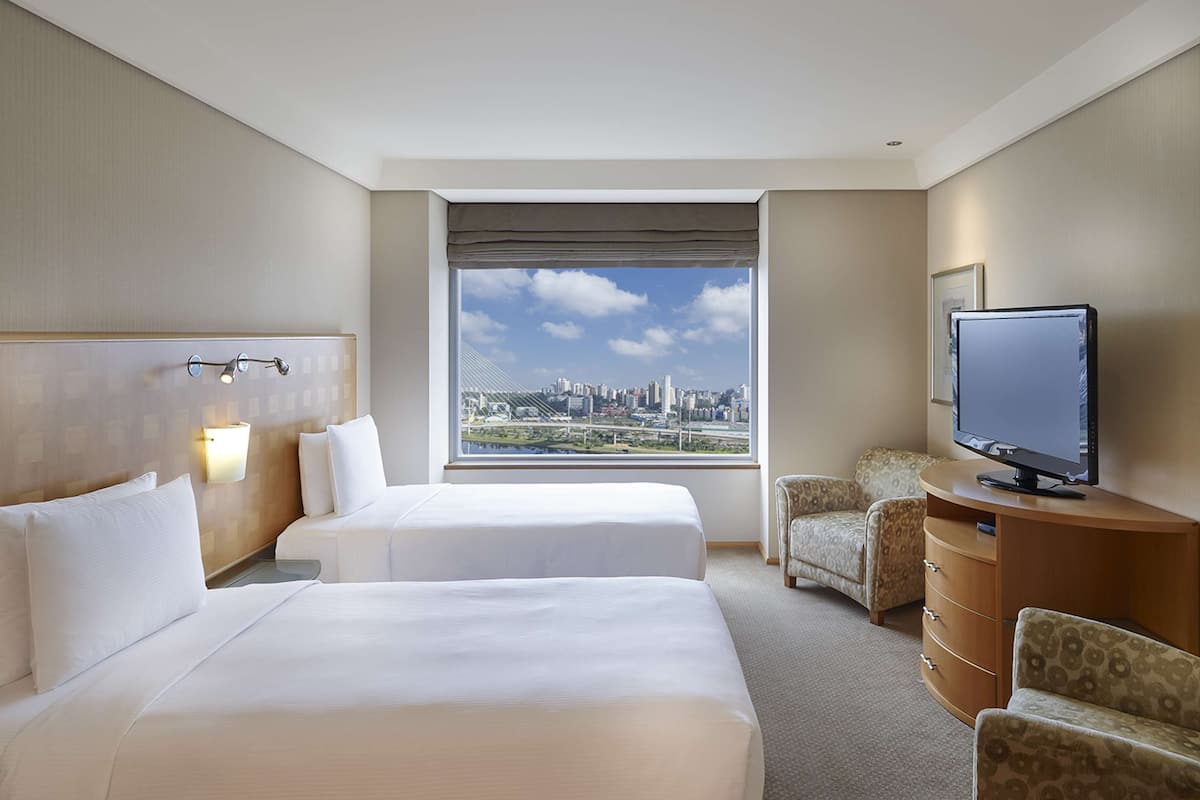 Habitación de hotel con dos camas, televisión, escritorio y vista a la ciudad.
