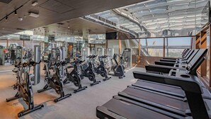 Een sportschool met cardioapparatuur, krachtstations en een groot raam met uitzicht op de stad.