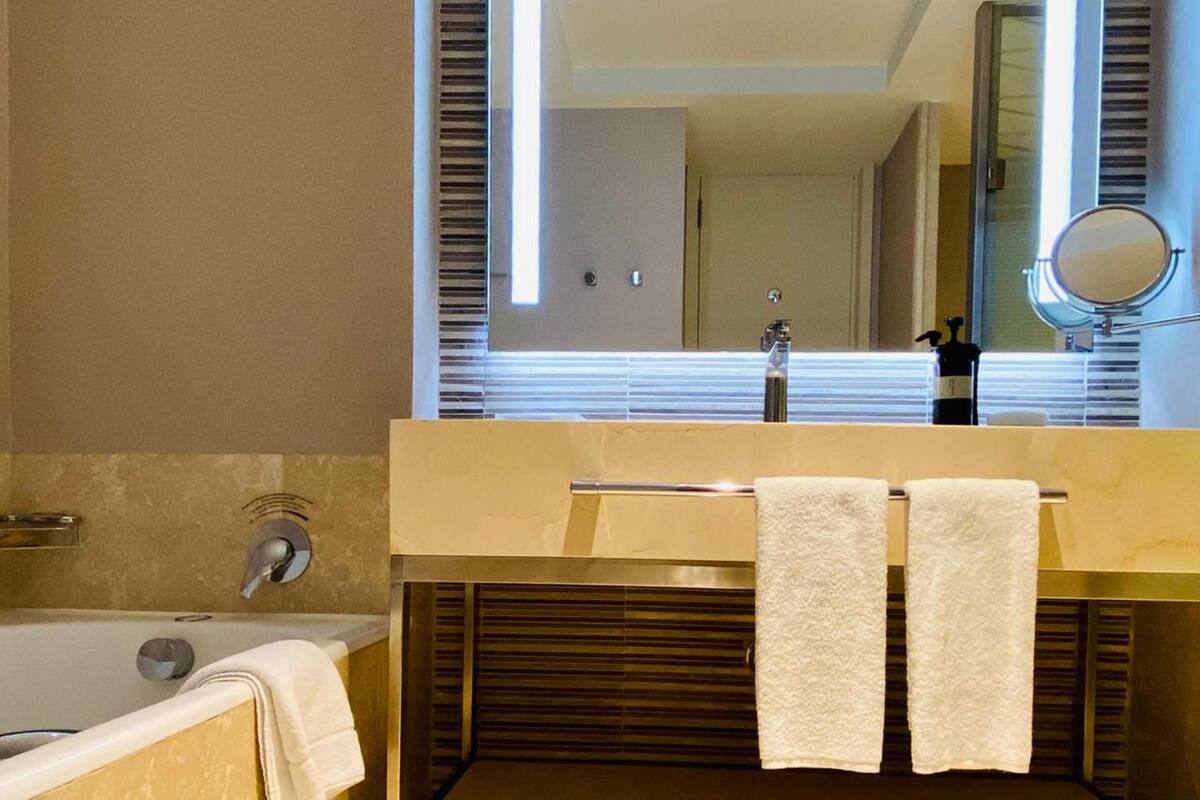 Un baño moderno con bañera, un lavabo con espejo y dos toallas colgadas en la pared.