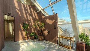 A spa area with a hot tub, wooden walls, potted plants, and a view of the city through large windows.