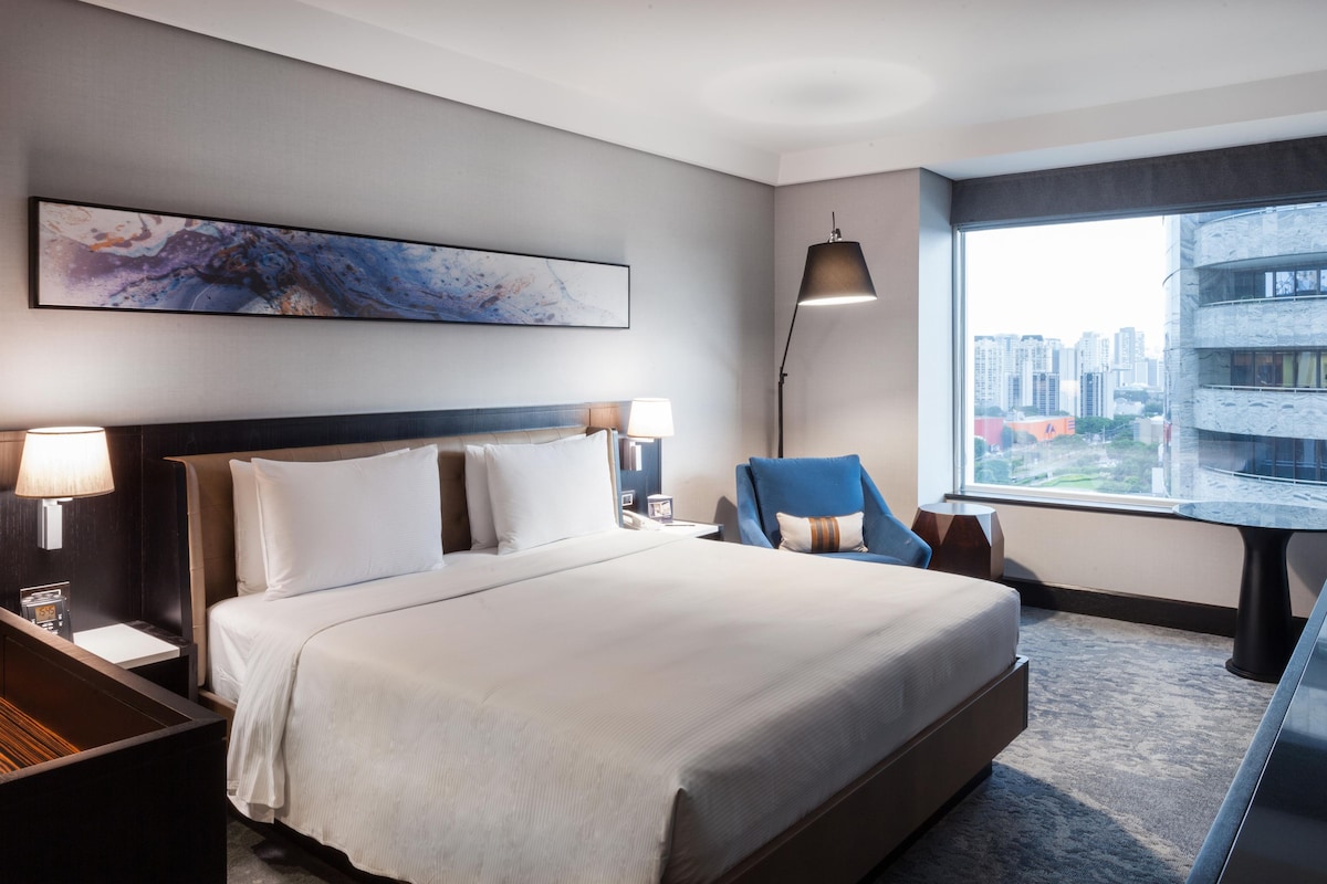 Een hotelkamer met een groot bed, een bureau, een stoel, een bureaulamp en een raam met uitzicht op de stad.