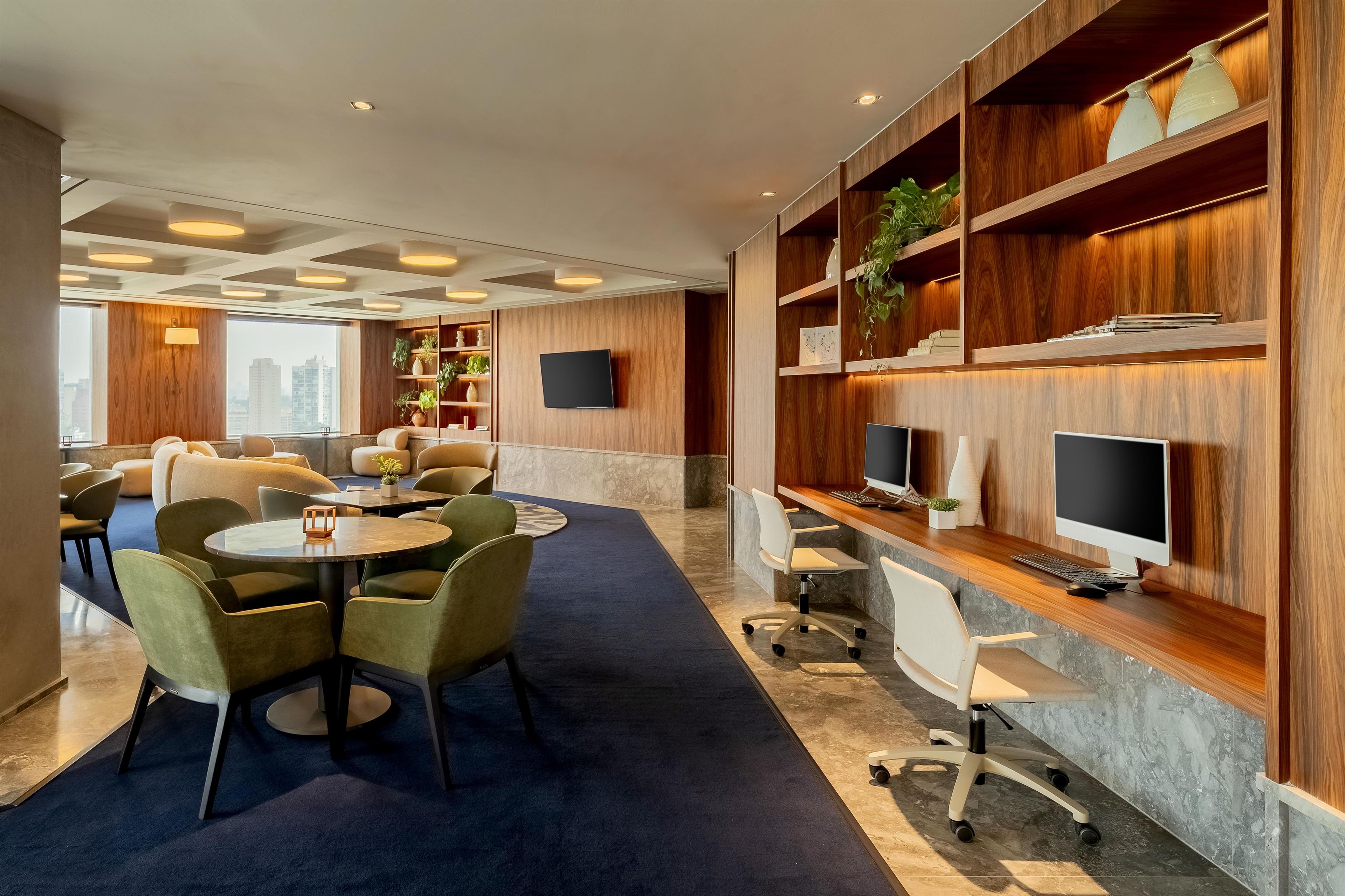 A modern hotel lobby with a seating area, a reception desk, and a large window offering a city view.