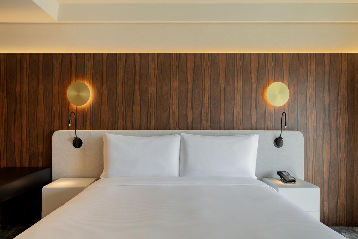 Een hotelkamer met een groot bed, twee nachtkastjes, een wandlamp en een telefoon.