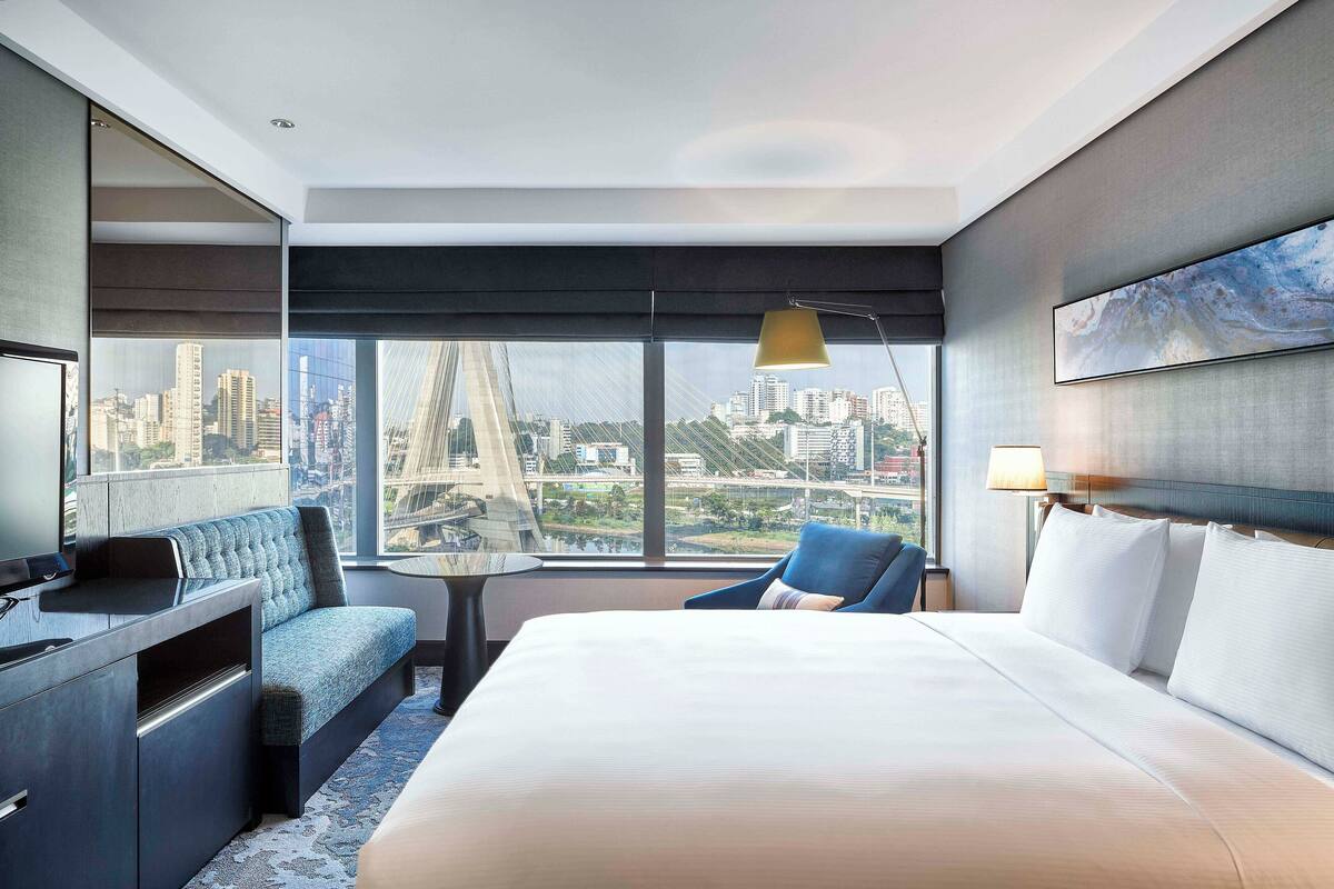 Habitación de hotel moderna con una cama grande, un escritorio, un sofá azul y vistas a la ciudad.