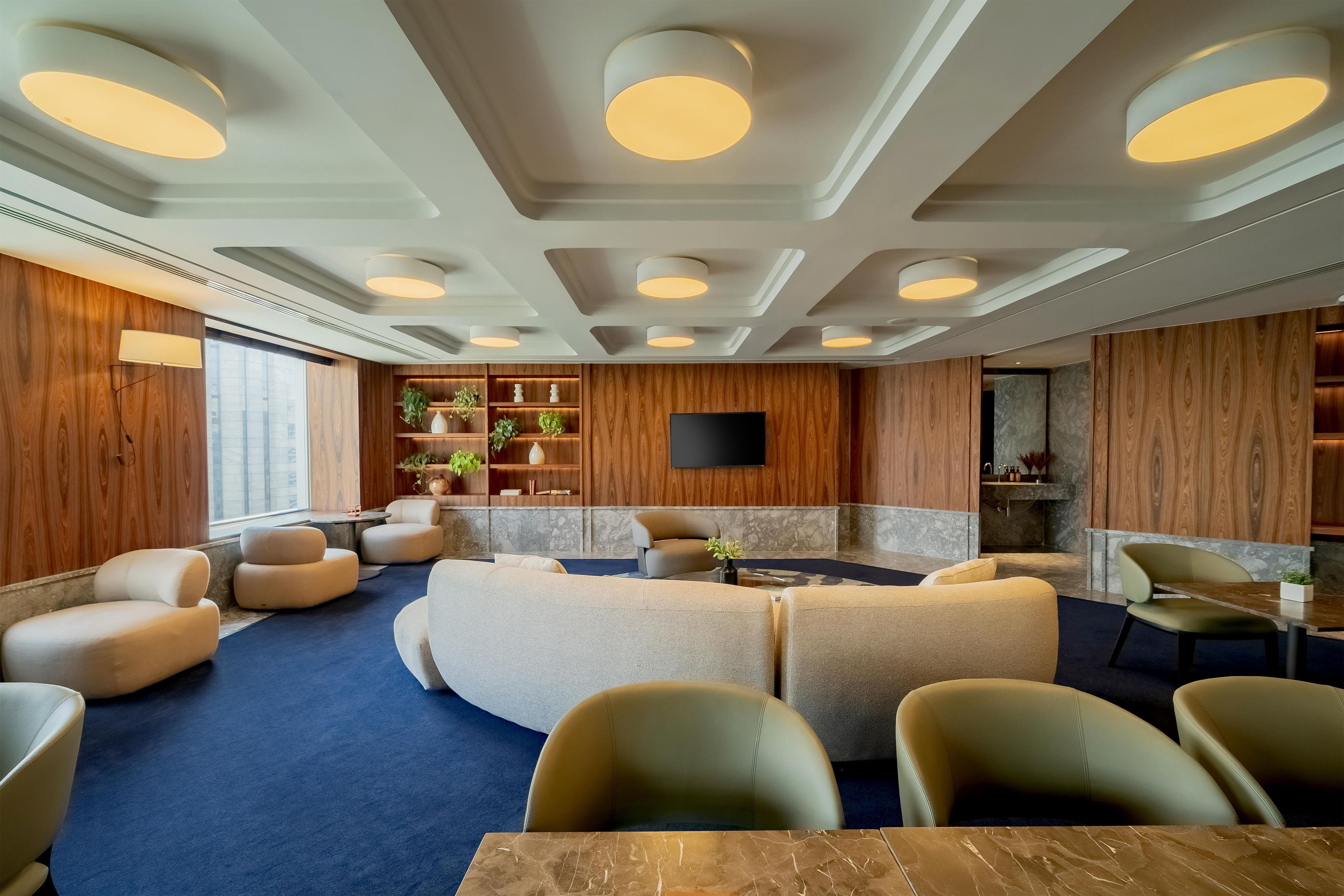 Un espace de détente moderne, doté de sièges confortables, d’un téléviseur à écran plat et de panneaux muraux en bois.