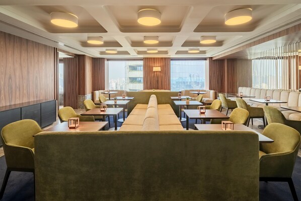 Un comedor moderno con asientos tipo cabina y mesas, ventanas amplias y vistas a la ciudad.