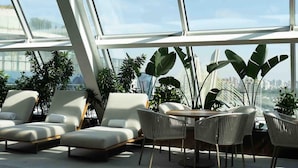 A modern indoor space with a glass ceiling, white furniture, and large potted plants.