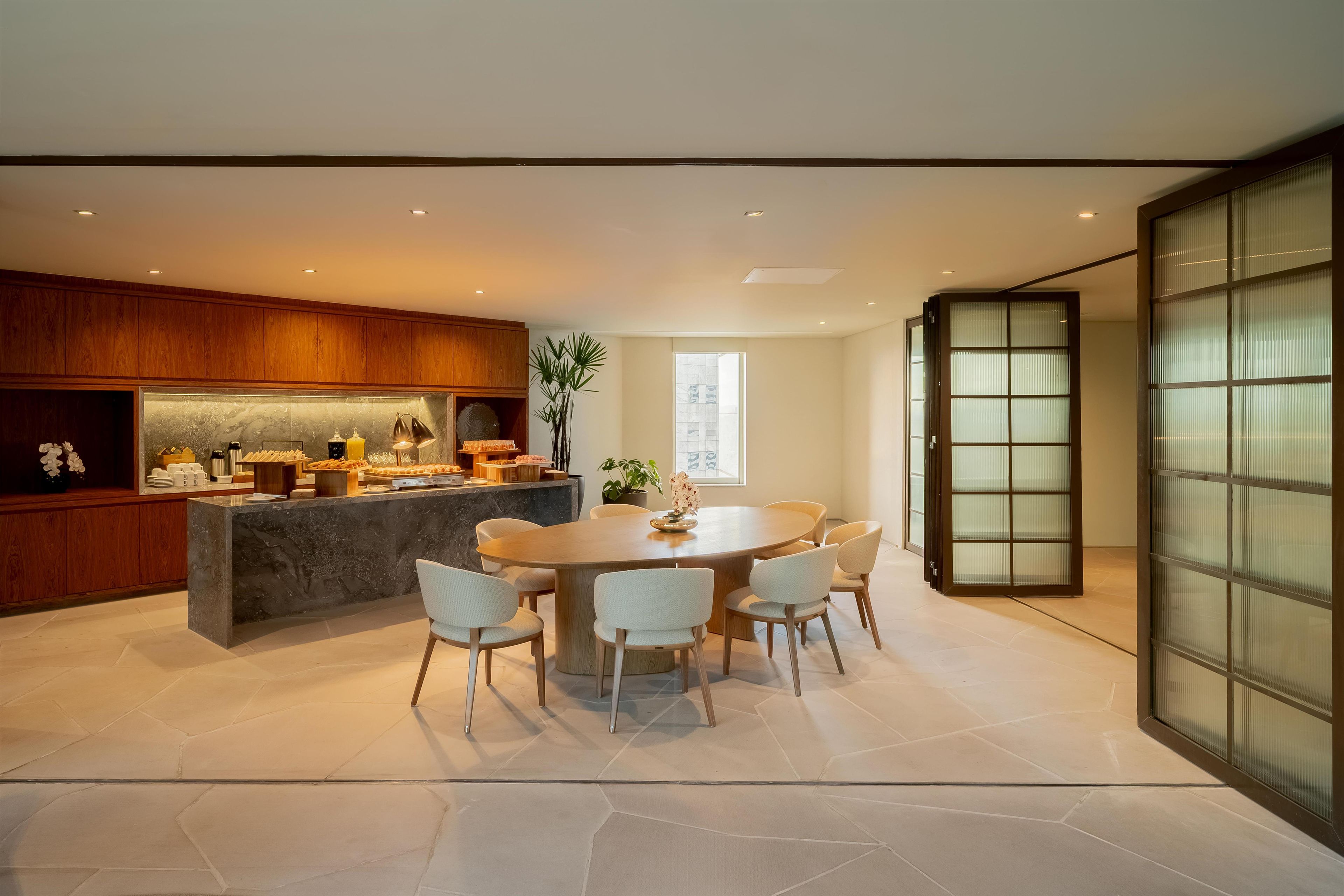 A modern kitchen with a central island, dining area with chairs, and a large window.